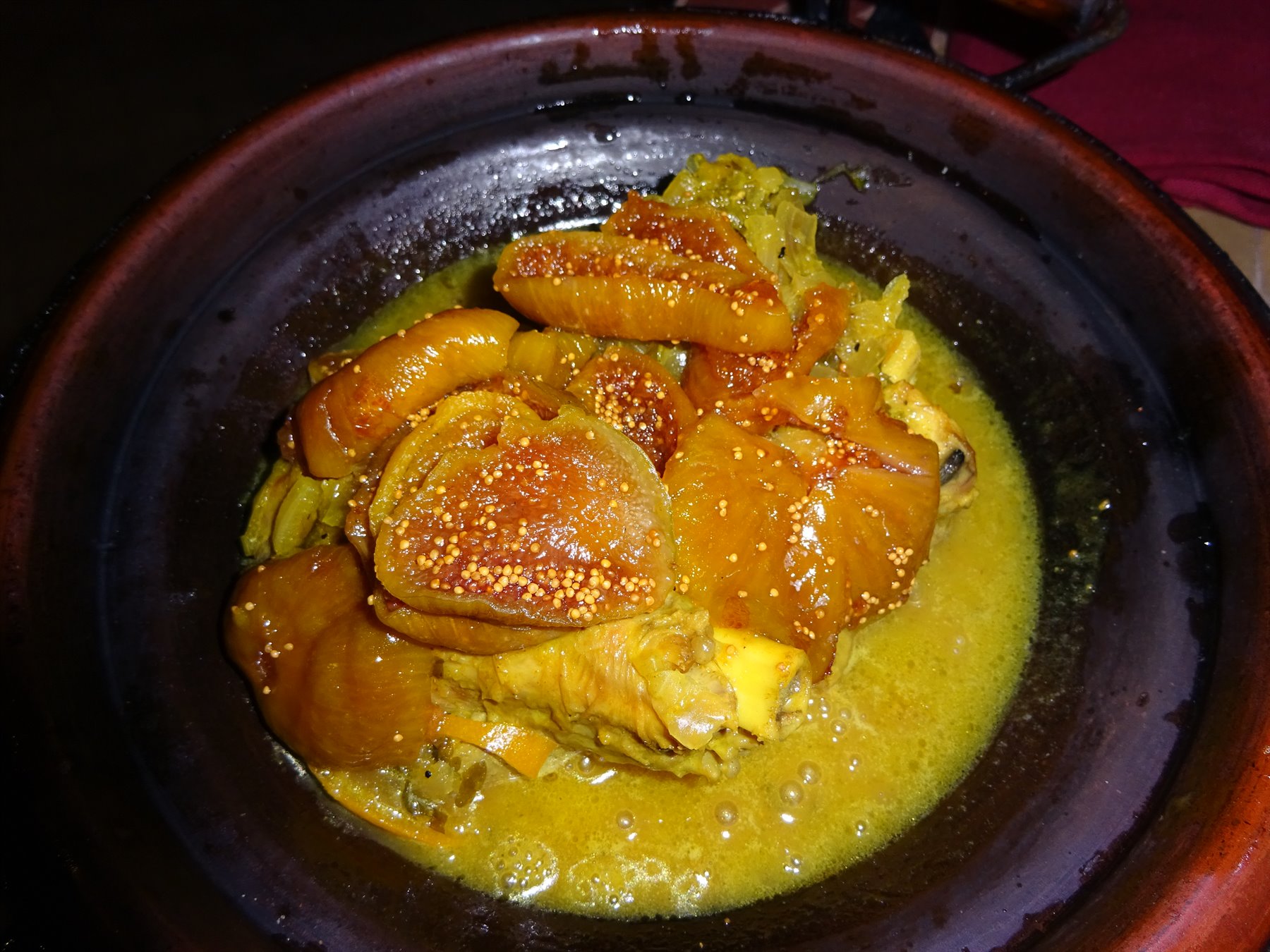 Tagine fumante nel piatto di terracotta, salse dorate e carne lucida
