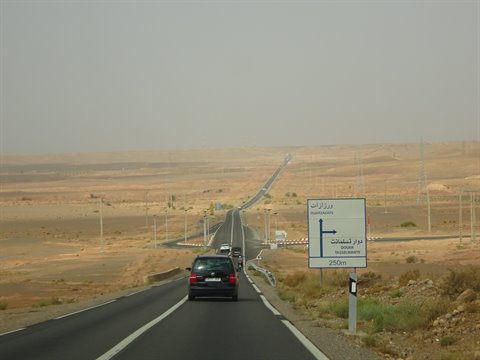 Auto sulla rettilineo desertico, cartello stradale con scritta araba e polvere