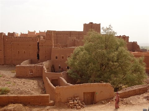 Raw-earth kasbah at Ait Ben Haddou, green tree and woman in pink