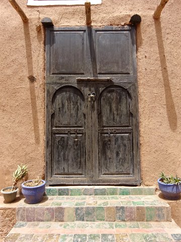 Dark wooden door on mud wall, potted plants and tiled steps, Marrakech