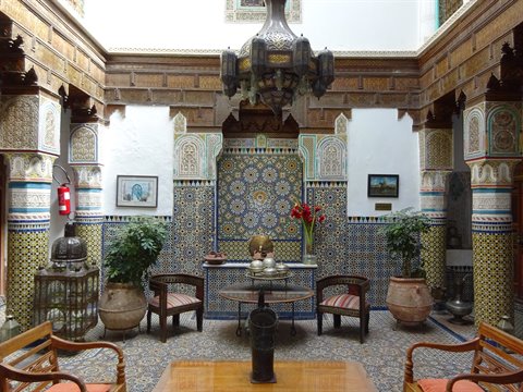 Riad a Fes, zellige colorato, lampadario in ottone, poltrone e piante intorno alla fontana