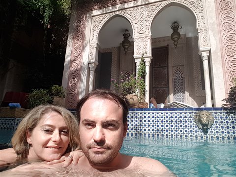 Coppia in piscina davanti ad archi intarsiati e lanterne, riad a Marrakech