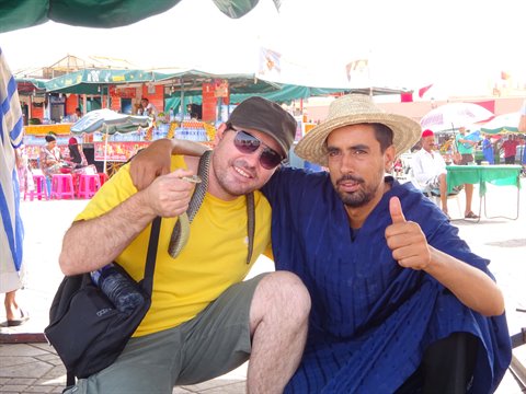 Tourist with snake and charmer in blue djellaba at Jamaa el Fna, Marrakech