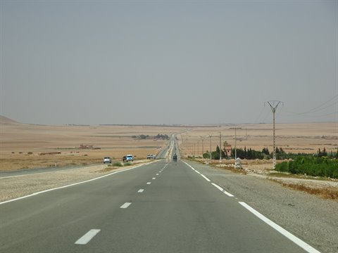 Straight desert highway toward Errachidia, cars and power poles among arid fields
