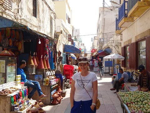 Tourist in Essaouira souk among stalls of pottery, spices and fruit