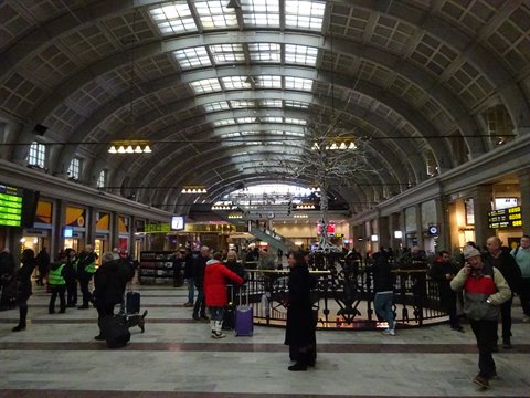 Travelers with luggage inside Stockholm Central Station, glass vaulted roof and lights