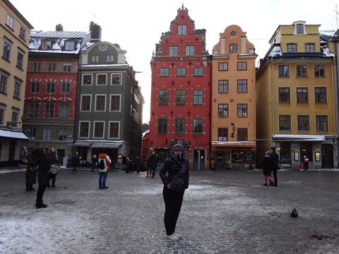 Smiling tourist posing in Stortorget square, Gamla Stan, snowy colorful houses