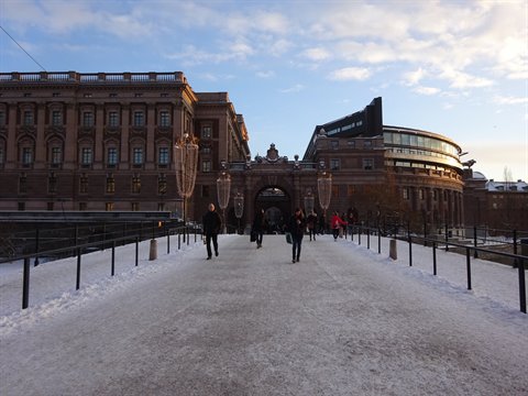 Pedestrians crossing snowy bridge toward the Riksdag in Stockholm, winter light