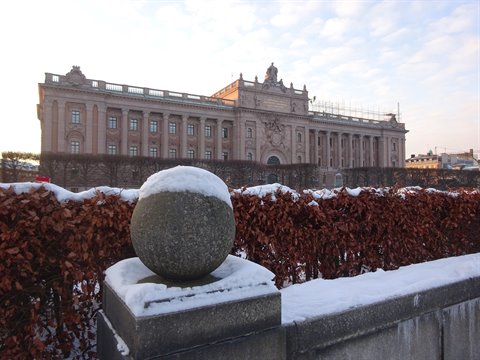 Snow-covered granite sphere before Stockholm's Riksdag parliament, brown hedges, winter light
