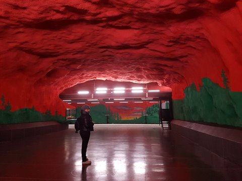 Traveler inside Solna Centrum station, red painted rock ceiling, Stockholm