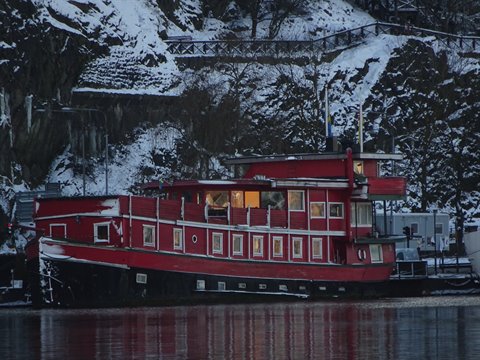 Red wooden tugboat moored in snowy Stockholm among rocks and warm lights