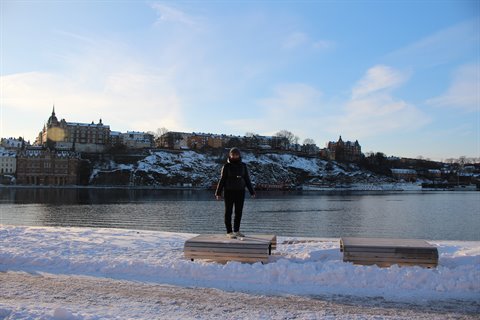 Woman standing on a snowy bench, historic Stockholm buildings across the water
