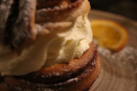 Cinnamon bun with whipped cream on wooden plate, warm light