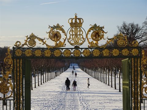 Golden crown gate at Drottningholm, people walking along snowy avenue