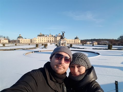 Couple selfie before snowy Drottningholm Palace, frozen gardens, blue sky