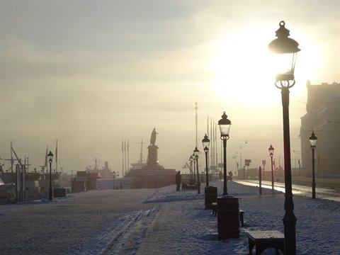 Snowy Skeppsbron quay in Stockholm, lampposts against hazy morning sun