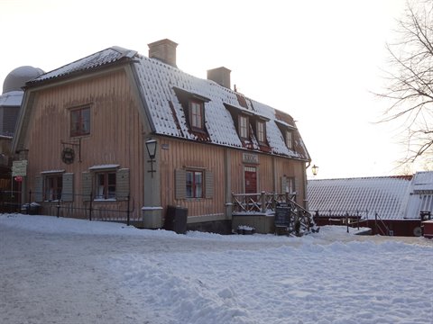 Snow-covered pink wooden house at Skansen, Stockholm, winter light