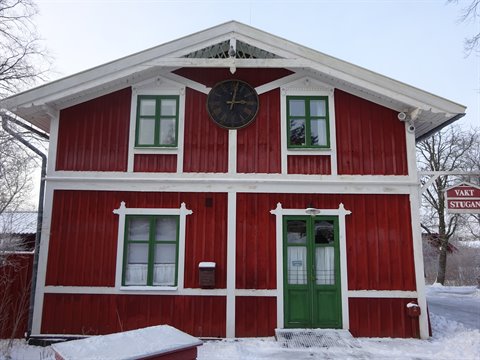 Red wooden house with clock and green windows in Stockholm snow