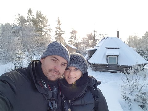 Couple selfie in front of a snow-covered wooden hut among frosted trees