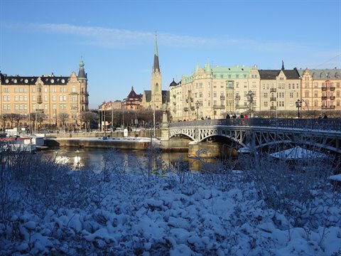 Bridge over icy water and snow, colorful buildings and spire in Stockholm