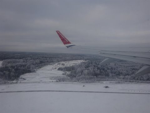 Airplane wing with red tail over snowy forests, landing in Stockholm