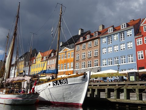 Historic boats moored at Nyhavn, colorful townhouses under cloudy sky