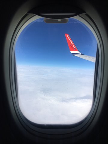 Norwegian's red wing seen from the airplane window above the clouds