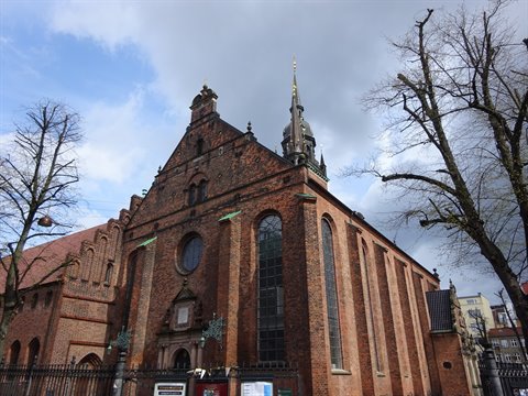 Red brick church with baroque spire, bare trees and cloudy sky