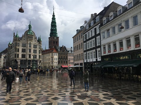 Amagertorv square in Copenhagen: wet mosaic pavement, green spire of St Nicholas, pedestrians