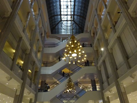 Interior atrium with golden chandeliers, escalators and marble walls under natural light
