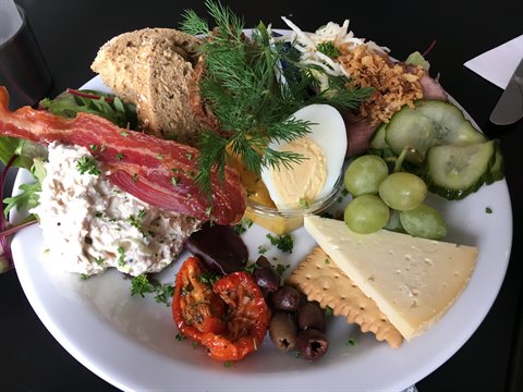 White plate with egg, bacon, cheese, olives, grapes and bread