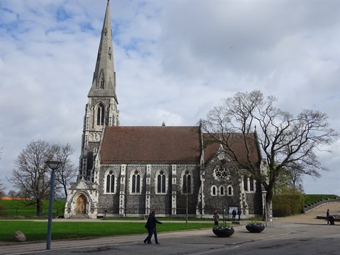 St Alban's Church in Copenhagen, grey stone Gothic spire among bare trees and passersby