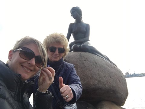Two tourists posing by the bronze Little Mermaid statue on the rock in Copenhagen