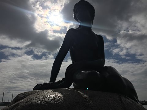 The Little Mermaid bronze statue silhouetted against a cloudy sky