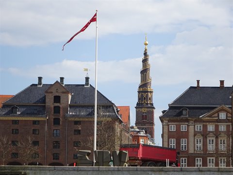 Copenhagen: spiral spire of Church of Our Saviour between brick buildings, red flag waving
