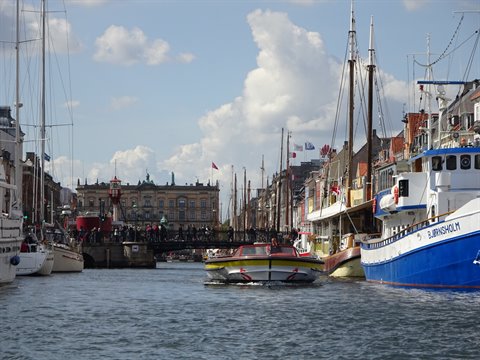 Tour boat sailing between moored ships along Nyhavn canal, Copenhagen