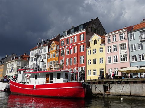 Nyhavn, Copenhagen: red boat moored in front of colorful townhouses under cloudy sky