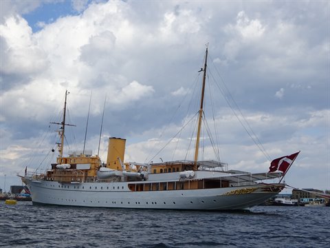 The Danish royal yacht Dannebrog, white with yellow funnel, flying the flag under cloudy skies