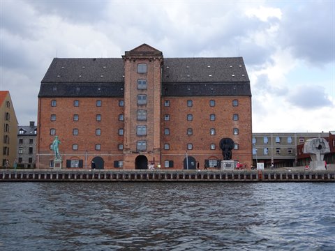 Red brick warehouse by the waterfront, sculptures along the quay, cloudy sky