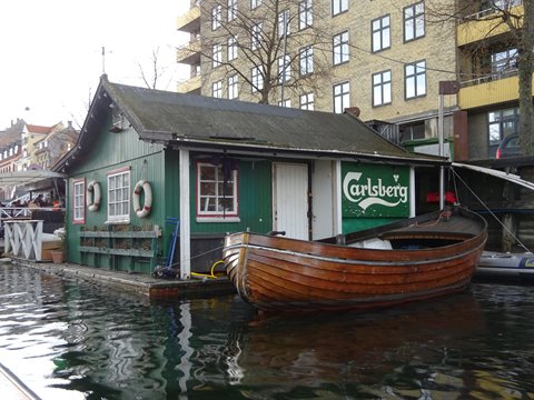Green floating wooden hut with Carlsberg sign and rowboat moored in Christiania, Copenhagen
