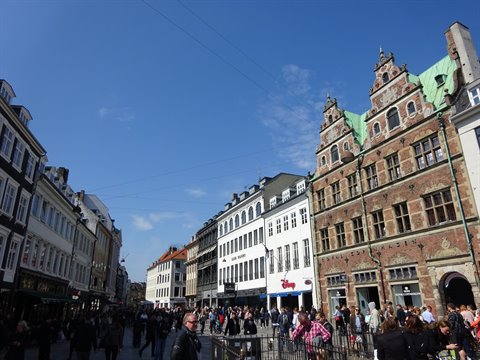 Crowd of pedestrians on a square between brick facades and colorful townhouses, blue sky