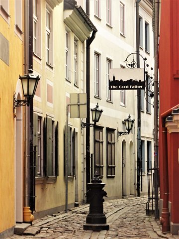 Cobblestone alley between colorful houses, black lanterns and The Good Father sign