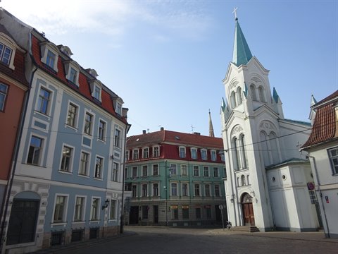 White church with green spire beside colorful buildings in Riga