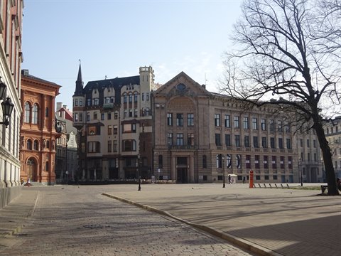 Sunlit square in Riga with brick and stone buildings, bare tree