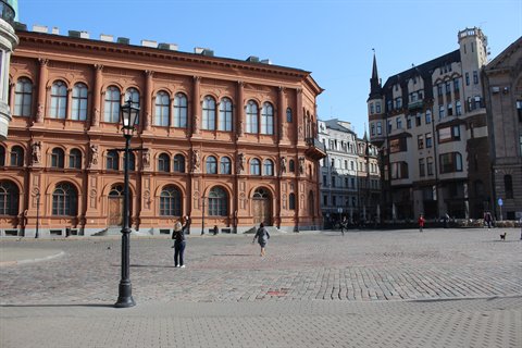Tourists on cobblestones in front of Riga's red Art Academy building