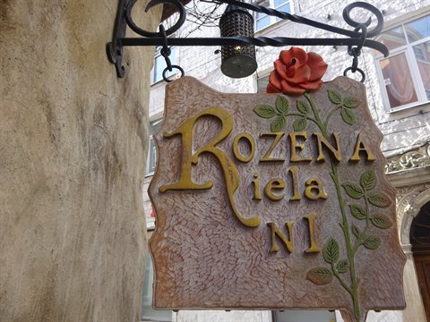 Stone shop sign with golden lettering Rožena, red rose and hanging lantern on facade