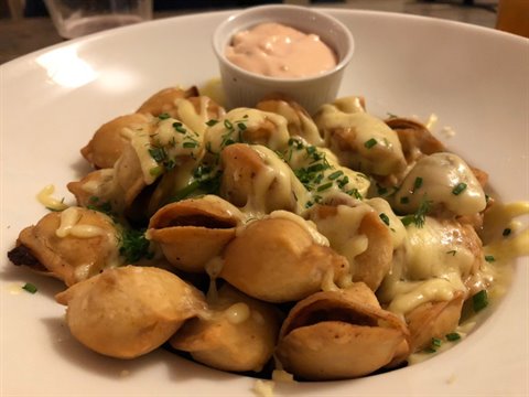 Tortellini with melted cheese and chives, pink sauce cup on white plate