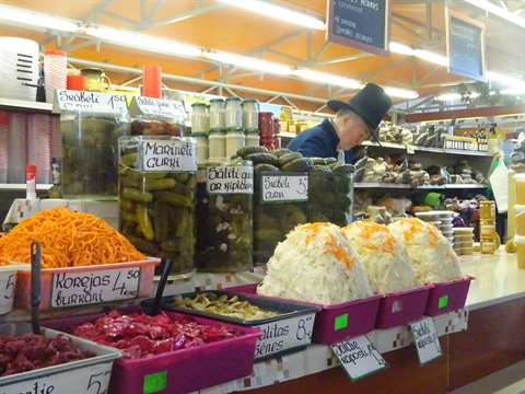 Vendor in hat at Riga Central Market among pickles, sauerkraut and carrots