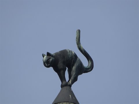Green-patina bronze cat statue arched on a spire against blue sky