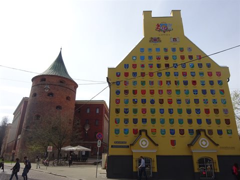 Medieval brick tower beside yellow facade covered with colorful coats of arms, Riga